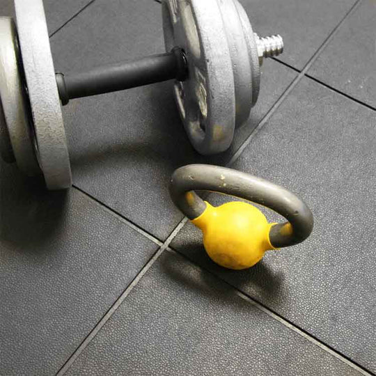 Dumbbell and kettlebell on black anti-fatigue rubber tiles in a gym