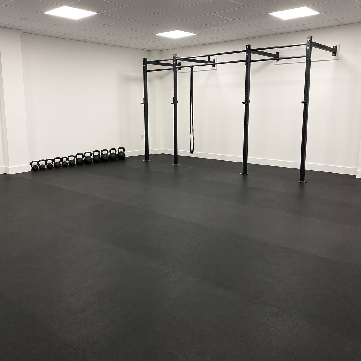 Black rubber gym flooring rolls seamlessly fitted wall-to-wall in a commercial gym with a pull-up rig