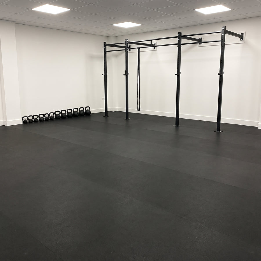 Black rubber gym flooring rolls seamlessly fitted wall-to-wall in a commercial gym with a pull-up rig