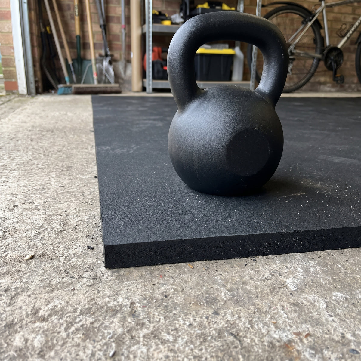 Black rubber gym flooring close-up showing the cut edge and thickness with a kettlebell