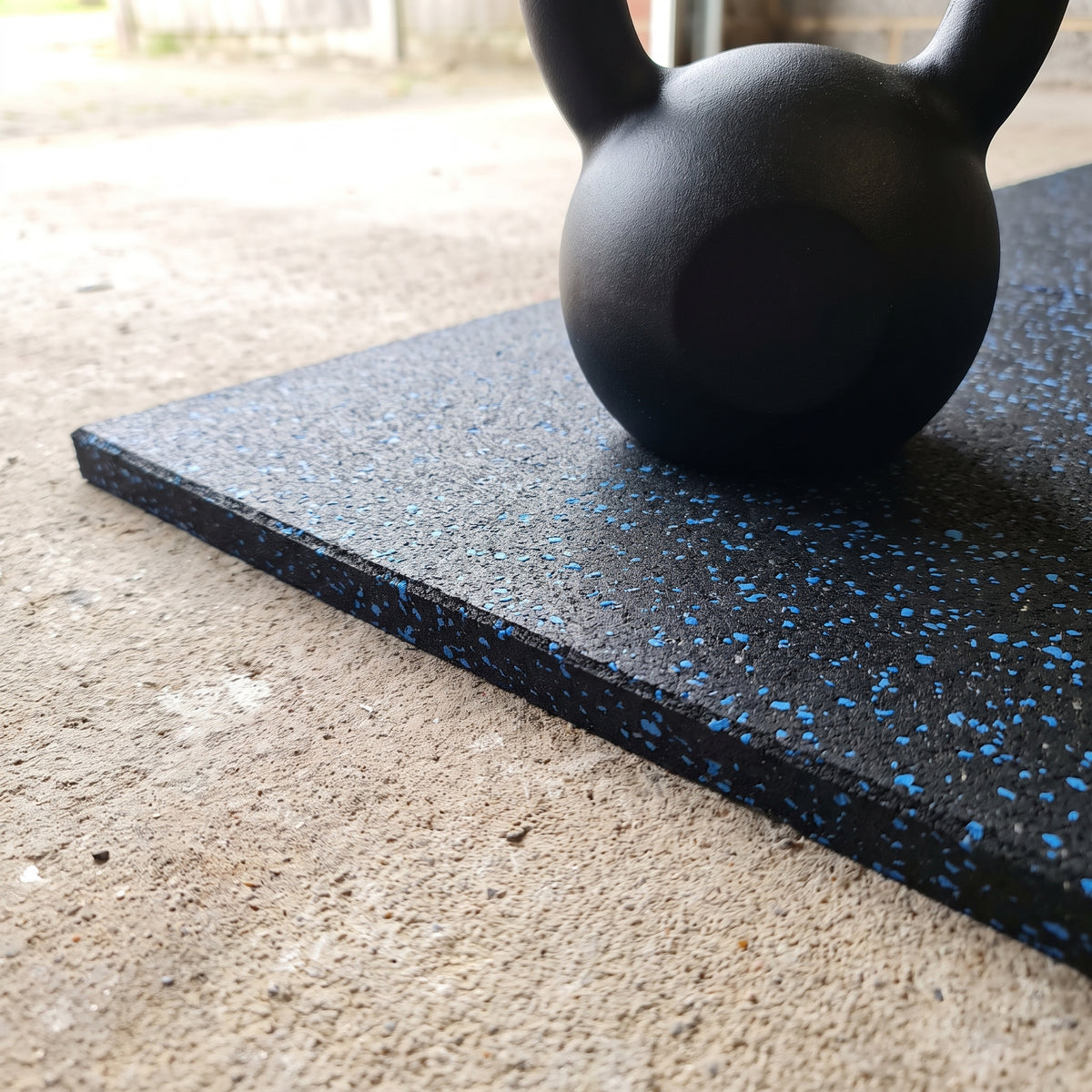 Blue Fleck rubber gym flooring close-up showing the cut edge and thickness with a kettlebell