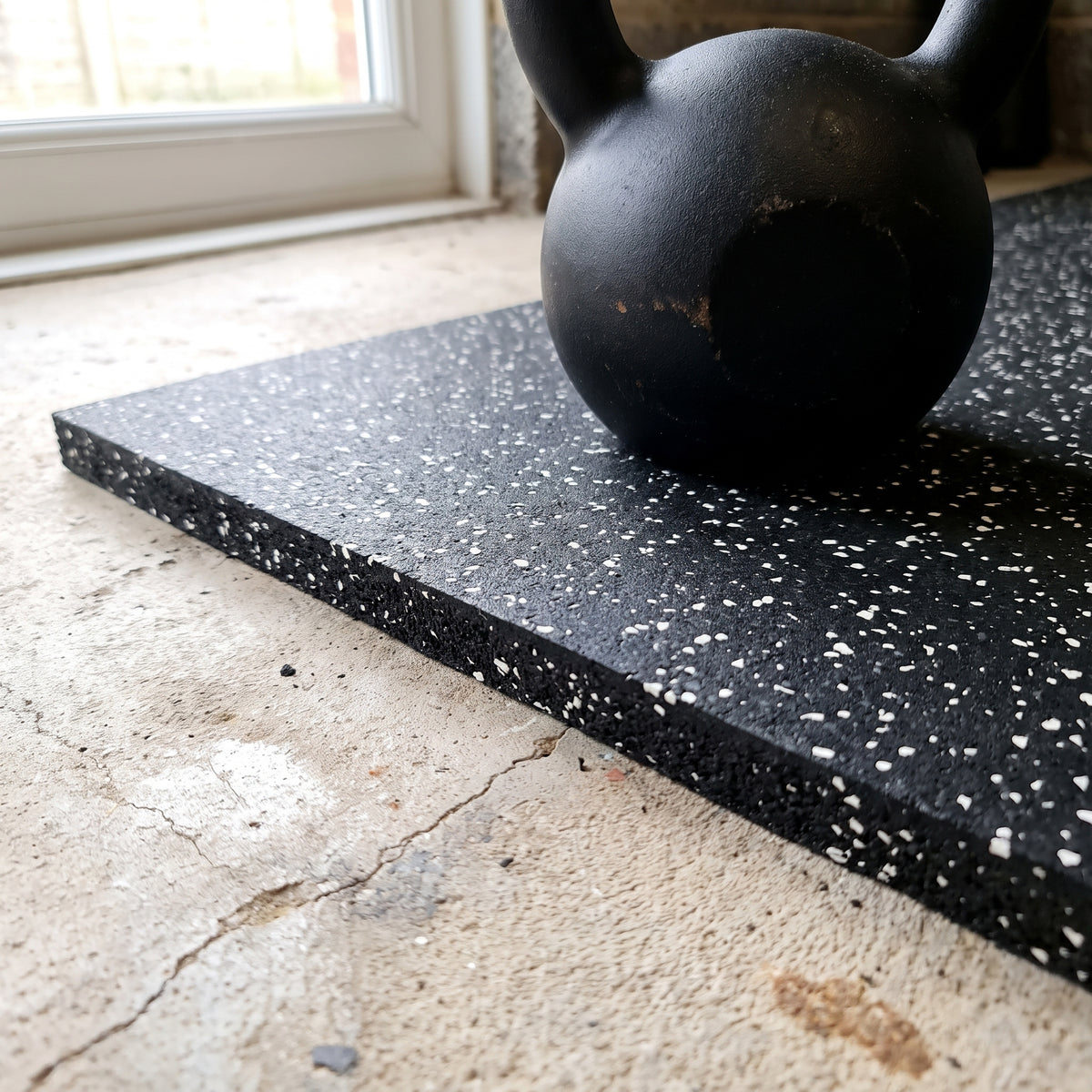 White Fleck rubber gym flooring close-up showing the cut edge and thickness with a kettlebell